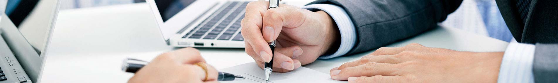 hands at a desk writing with a computer in the background